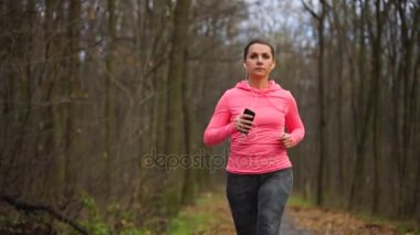 Kadının bir sonbahar orman günbatımında çalışan akıllı telefon ve kulaklık ile yakın çekim