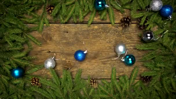 Decoraciones navideñas que caen sobre un fondo de madera con ramas de abeto y conos listos para su diseño. Vacaciones de invierno fondo — Vídeo de stock