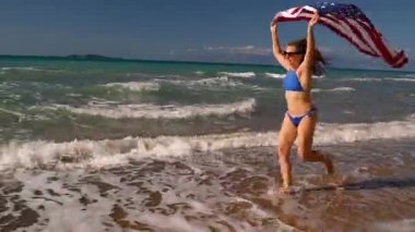 Bikini kadın bizimle bayrağı sahilde su çalışan plaj. Bağımsızlık günü ABD kavramı.