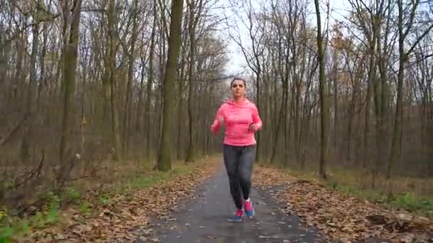 Primer plano de la mujer con auriculares y smartphone corriendo a través de un bosque otoñal al atardecer — Vídeos de Stock