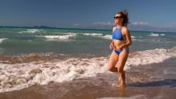 Bikini de playa mujer despreocupada corriendo por el agua en la playa. Pintoresca costa marítima de Corfú, Grecia . — Vídeo de stock