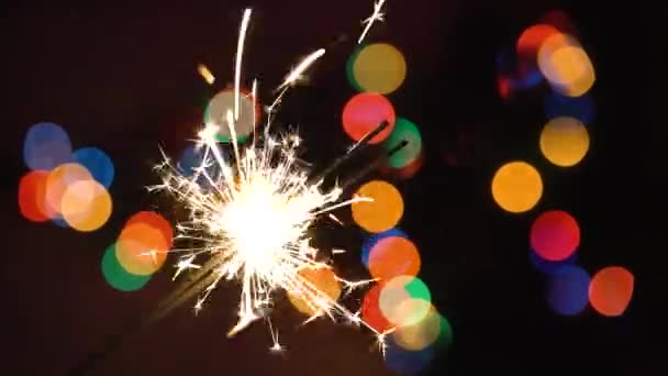 Kerst sparkler branden op de achtergrond van een kerstboom met kleurrijke bokeh en kerst verlichting — Stockvideo
