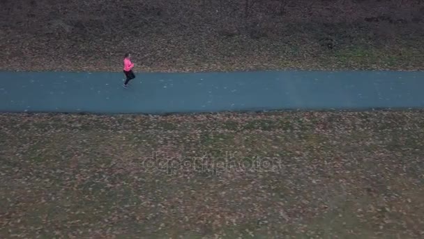 Вид с воздуха на женщину, бегущую через осенний лес на закате — стоковое видео