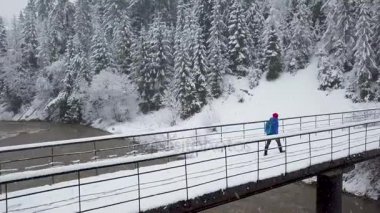 Kar fırtınasında bir karlı dağ iğne yapraklı orman ve kız bir dağ nehir kenarında bir dağ arasında bir köprü yürüyüş üzerinde uçuş ile iğne yapraklı orman kışın kapalı.
