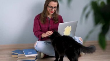 Dizüstü bilgisayar kullanarak, bir kedi okşayarak ve yere evde oturmak güzel kız