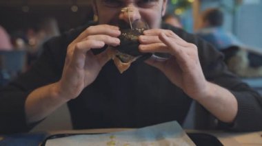 Adam bir kafede hamburger yiyor