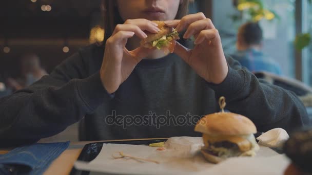 Mujer come una hamburguesa en un café — Vídeos de Stock