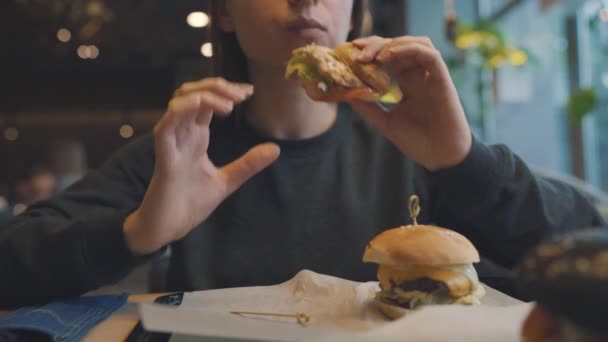 Vrouw eet een hamburger in een café — Stockvideo