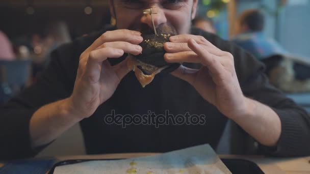 L'uomo mangia un hamburger in un caffè — Video Stock