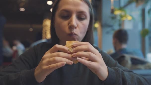 Vrouw eet een hamburger in een café — Stockvideo