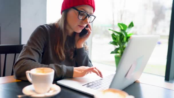 Hermosa joven mujer trabajando y hablando en un teléfono inteligente en un café — Vídeos de Stock