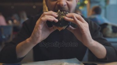 Adam bir kafede hamburger yiyor
