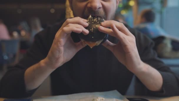 El hombre come una hamburguesa en un café — Vídeos de Stock