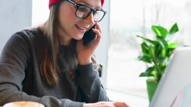 Hermosa joven mujer trabajando y hablando en un teléfono inteligente en un café — Vídeos de Stock