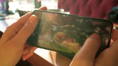 Kız bir fotoğraf yemek smartphone cep telefonu ile bir kafede yakın yapar