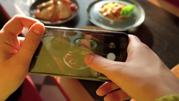Meisje maakt een foto van de maaltijd op een smartphone in een café close-up — Stockvideo