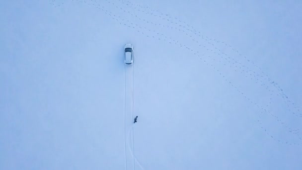 View from height to man is riding a snowboard on a snow-covered field on a cable behind a car — Stock Video