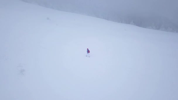 Flight over the lonely tourist girl walking along the top of a mountain covered with snow. Uncomfortable unfriendly winter weather. — Stock Video