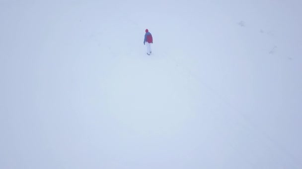 Volo sopra la ragazza turistica solitaria che cammina lungo la cima di una montagna coperta di neve. Tempo scomodo sfavorevole inverno . — Video Stock