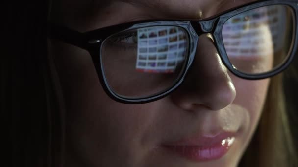 Woman in glasses looking on the monitor and surfing Internet. The monitor screen is reflected in the glasses — Stock Video