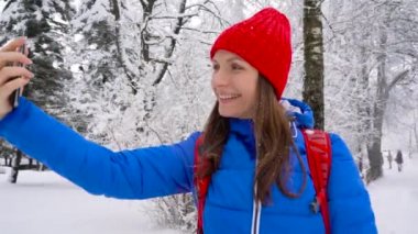 Genç kadın bir smartphone için yapmak kendi fotoğraflarını karla kaplı bir güzel kış manzara kullanır