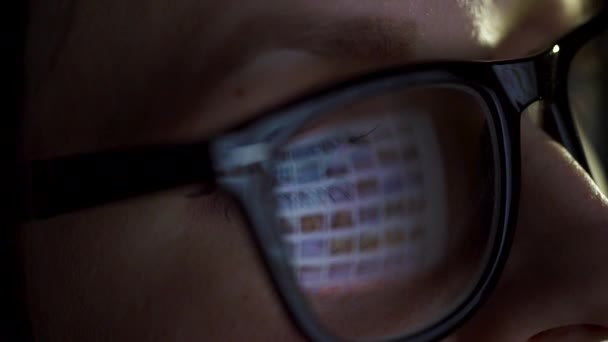 Woman in glasses looking on the monitor and surfing Internet. The monitor screen is reflected in the glasses — Stock Video