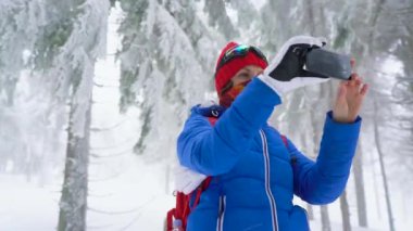 Yalnız turist kız kış karla kaplı iğne yapraklı bir ormanda dağlarda yürüyüş ve doğa fotoğrafı Smartphone'da alır. Soğuk hava