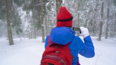 Yalnız turist kız kış karla kaplı iğne yapraklı bir ormanda dağlarda yürüyüş ve doğa fotoğrafı Smartphone'da alır. Soğuk hava