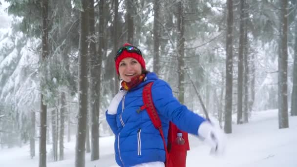 Divertida turista saludando a alguien y caminando en un bosque de coníferas cubierto de nieve en las montañas. Clima helado. Movimiento lento — Vídeo de stock