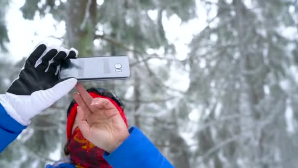 외로운 관광 여 자가 산에 겨울 눈 덮인 침 엽 수 숲에 산책 스마트폰에 자연의 사진을 걸립니다. 서리가 내린 날씨입니다. 슬로우 모션 — 비디오