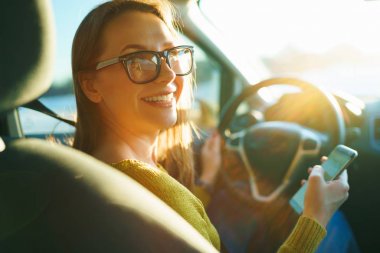 Günbatımında bir araba sürüş sırasında bir smartphone kadın gözlük kullanır