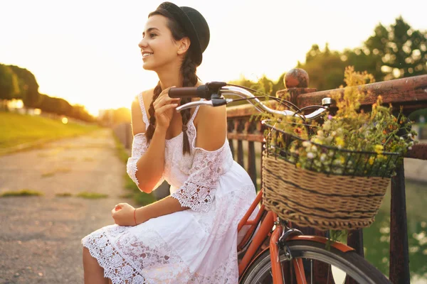 Νεαρή όμορφη γυναίκα που κάθεται με το ποδήλατο με λουλούδια στο ήλιο — Φωτογραφία Αρχείου