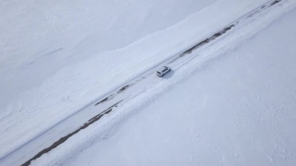 Aerial view on car driving through winter forest road between the snow-covered fields — Stock Video