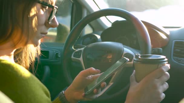 Mujer en vasos usando un teléfono inteligente y bebe café en el coche — Vídeo de stock