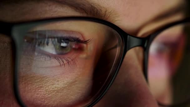 Mujer con gafas mirando en el monitor y navegando por Internet. La pantalla del monitor se refleja en las gafas — Vídeo de stock