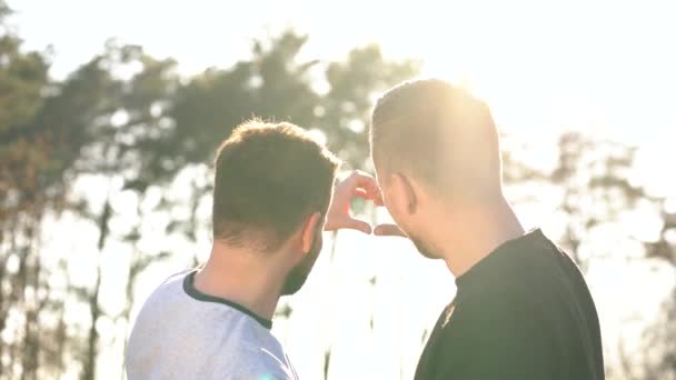 Jovem gay casal fazendo coração símbolo com suas mãos no por do sol ao ar livre — Vídeo de Stock