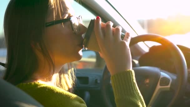 Frau mit Brille bedient Smartphone und trinkt Kaffee im Auto — Stockvideo