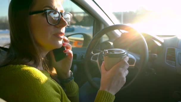 メガネの女はスマート フォンで話す、車の中でコーヒーを飲む — ストック動画