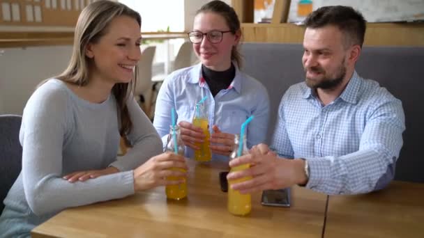 Tre vänner sitta på ett café, dricka juice och ha kul kommunicera — Stockvideo