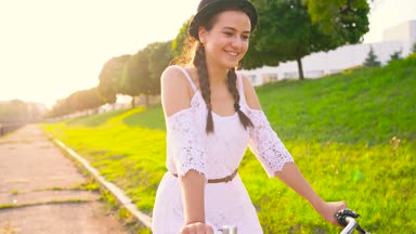 Genç güzel kadın günbatımında bir bisiklet sürme. Ağır çekim