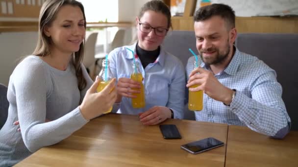 Drei Freunde sitzen in einem Café, trinken Saft und haben Spaß an der Kommunikation — Stockvideo