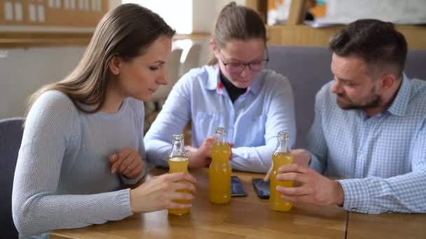 Tres amigos se sientan en un café, beben jugo y se divierten comunicándose — Vídeos de Stock