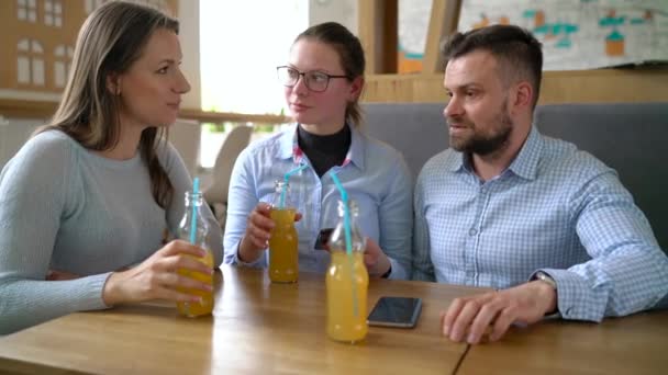 Trois amis s'assoient dans un café, boivent du jus et s'amusent à communiquer — Video