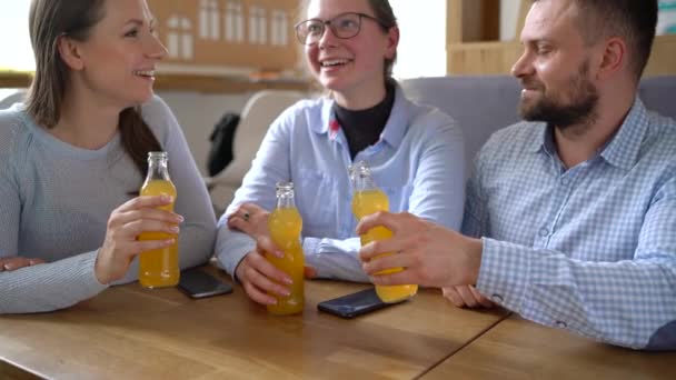 Трое друзей сидят в кафе, пьют сок и весело общаются — стоковое видео