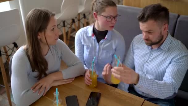 Tre vänner sitta på ett café, dricka juice och ha kul kommunicera — Stockvideo