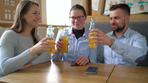 Tre amici si siedono in un caffè, bevono succo e si divertono a comunicare — Video Stock
