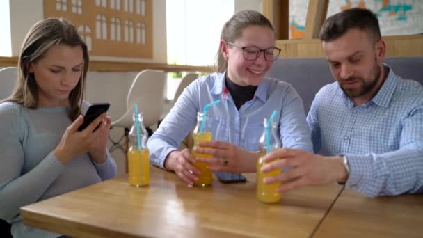 Três amigos se sentam em um café, bebem suco e se divertem se comunicando — Vídeo de Stock