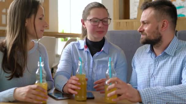 Drei Freunde sitzen in einem Café, trinken Saft und haben Spaß an der Kommunikation — Stockvideo