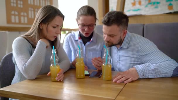Trois amis s'assoient dans un café, boivent du jus et s'amusent à communiquer — Video