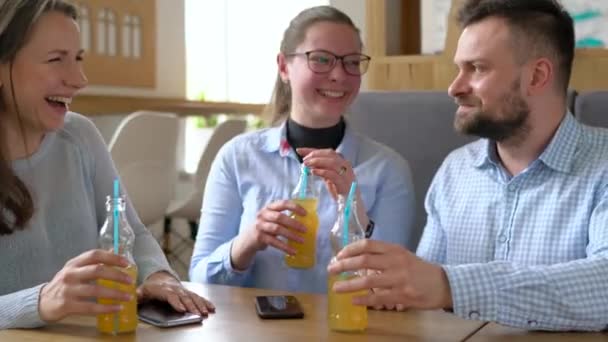 Drei Freunde sitzen in einem Café, trinken Saft und haben Spaß an der Kommunikation — Stockvideo